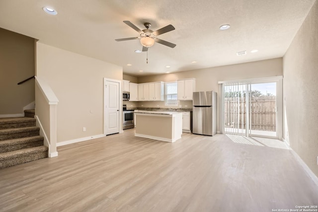 kitchen with a center island, white cabinets, ceiling fan, light wood-type flooring, and appliances with stainless steel finishes