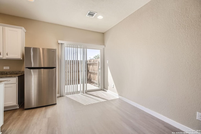 kitchen featuring stainless steel fridge, light wood-type flooring, and white cabinetry