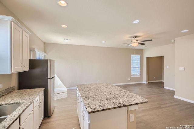 kitchen with white cabinets, a kitchen island, light stone countertops, and ceiling fan