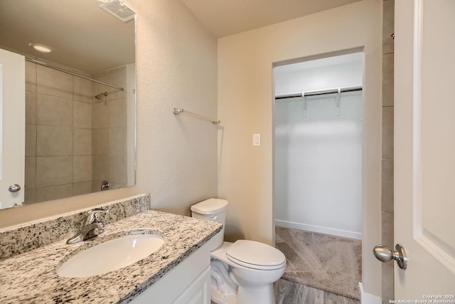 bathroom featuring tiled shower, vanity, hardwood / wood-style flooring, and toilet