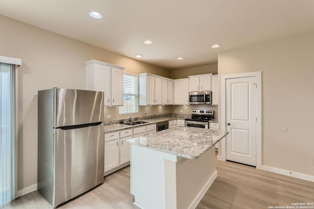 kitchen with white cabinets, a kitchen island, light stone counters, and appliances with stainless steel finishes