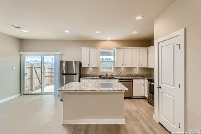 kitchen featuring light stone countertops, appliances with stainless steel finishes, sink, white cabinets, and a center island