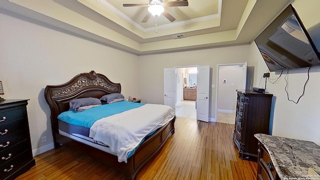 bedroom featuring connected bathroom, ceiling fan, crown molding, wood-type flooring, and a tray ceiling