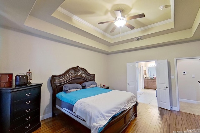 bedroom with a tray ceiling, ensuite bathroom, crown molding, and ceiling fan