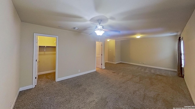 unfurnished bedroom with a walk in closet, a closet, ceiling fan, and carpet floors