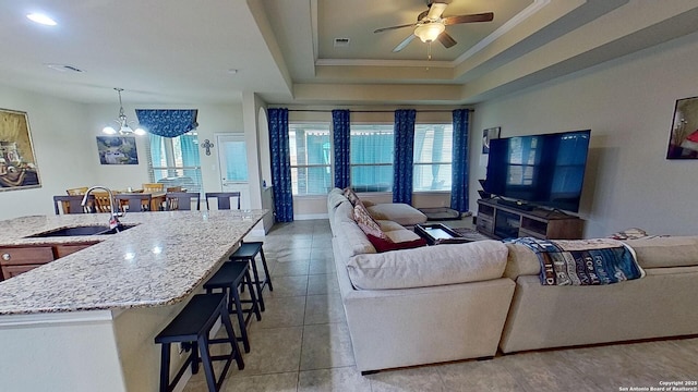 living room featuring sink, a tray ceiling, light tile patterned flooring, ceiling fan with notable chandelier, and ornamental molding