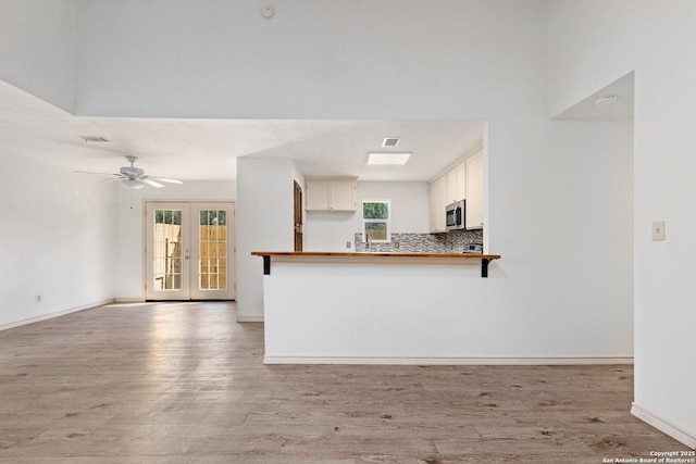 kitchen with decorative backsplash, light hardwood / wood-style floors, kitchen peninsula, and french doors