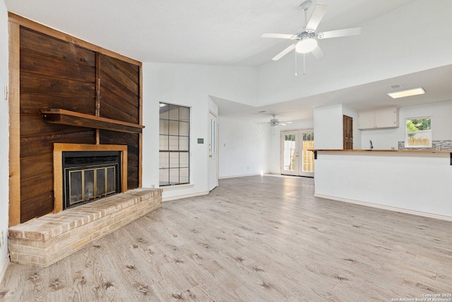 unfurnished living room featuring vaulted ceiling, light hardwood / wood-style floors, a brick fireplace, and ceiling fan