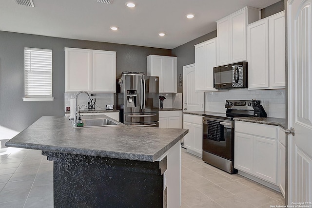 kitchen with white cabinets, appliances with stainless steel finishes, a kitchen island with sink, and sink