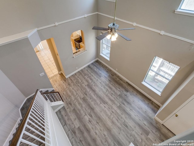 unfurnished living room featuring ceiling fan, a high ceiling, and light wood-type flooring