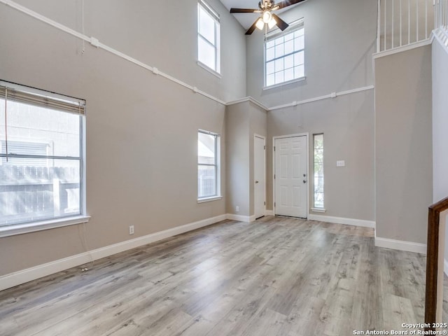 entrance foyer featuring ceiling fan, plenty of natural light, a towering ceiling, and light hardwood / wood-style flooring