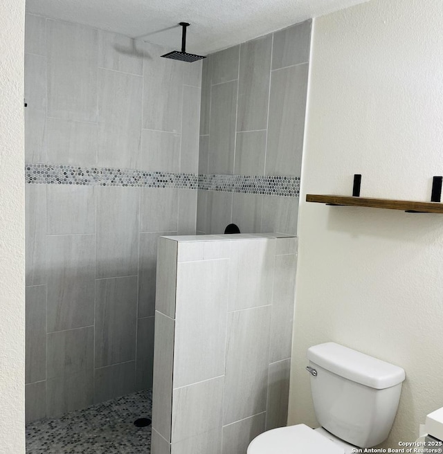 bathroom featuring a tile shower, vanity, a textured ceiling, and toilet