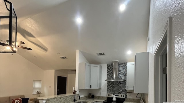 kitchen featuring light stone countertops, white cabinetry, lofted ceiling, and wall chimney range hood