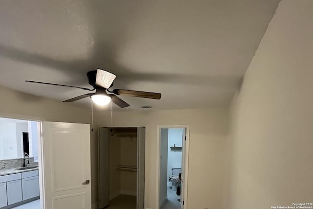 interior space with a closet, connected bathroom, ceiling fan, and sink