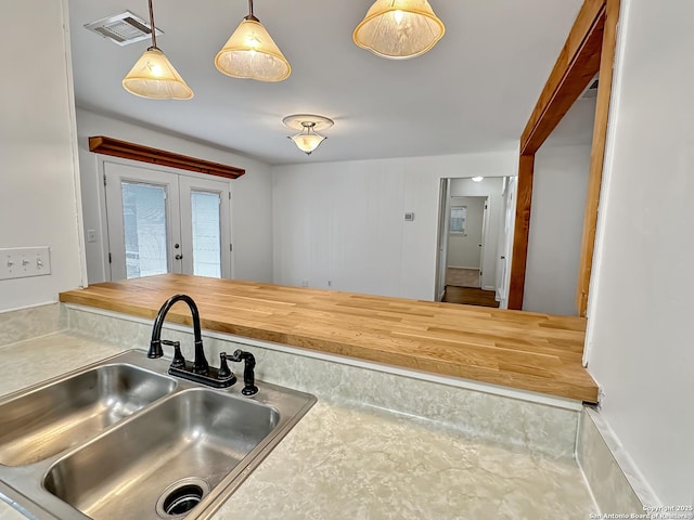 kitchen featuring pendant lighting, butcher block countertops, sink, and french doors