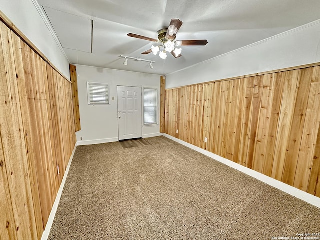 spare room featuring carpet, track lighting, ceiling fan, and wooden walls