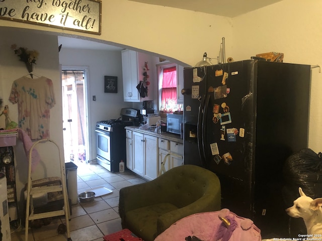 kitchen featuring range with gas stovetop, light tile patterned flooring, black fridge, and white cabinetry