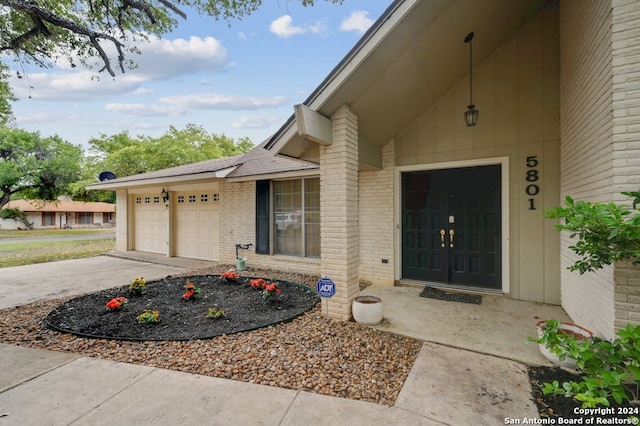 entrance to property featuring driveway, an attached garage, and brick siding