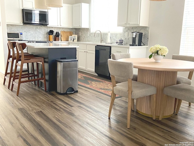 kitchen featuring dishwasher, a kitchen island, hardwood / wood-style floors, a breakfast bar, and white cabinets