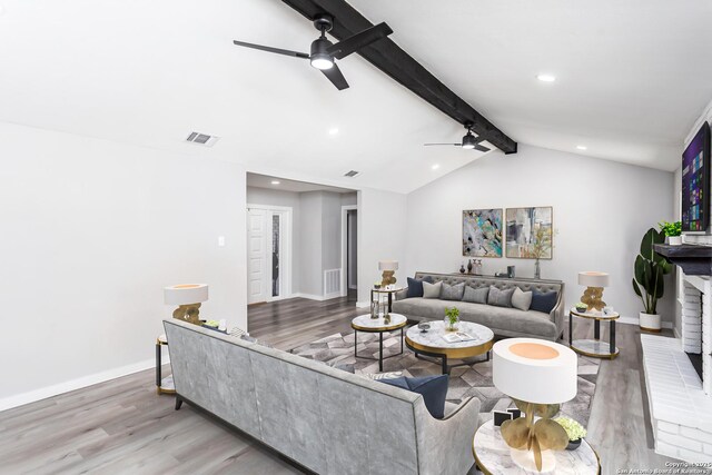 living room featuring ceiling fan, lofted ceiling with beams, light wood-type flooring, and a brick fireplace