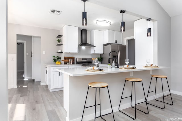 kitchen with a kitchen breakfast bar, stainless steel appliances, wall chimney range hood, light hardwood / wood-style flooring, and white cabinets