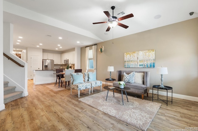 living room with ceiling fan, light hardwood / wood-style floors, and vaulted ceiling