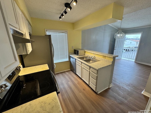 kitchen featuring sink, a textured ceiling, decorative light fixtures, appliances with stainless steel finishes, and light wood-type flooring