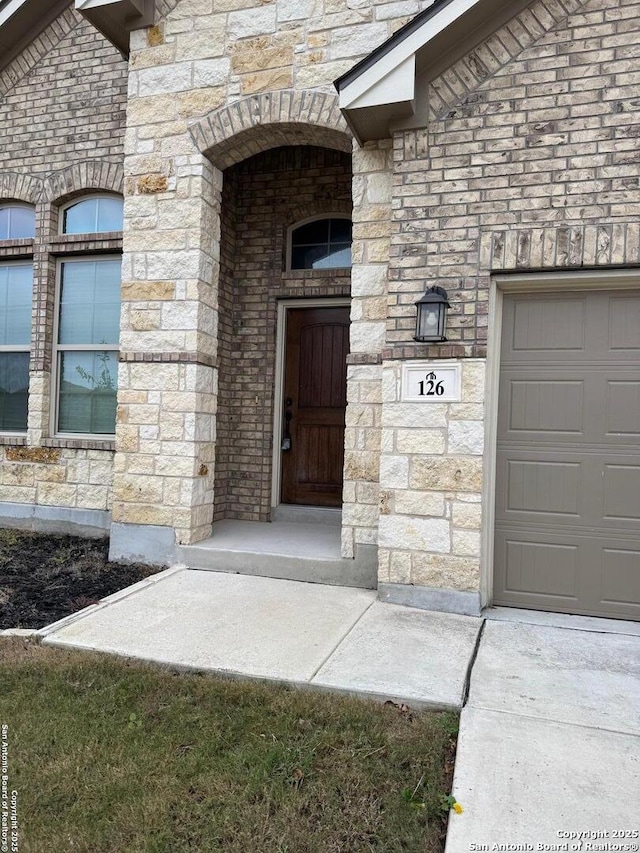 doorway to property with a garage, stone siding, and brick siding