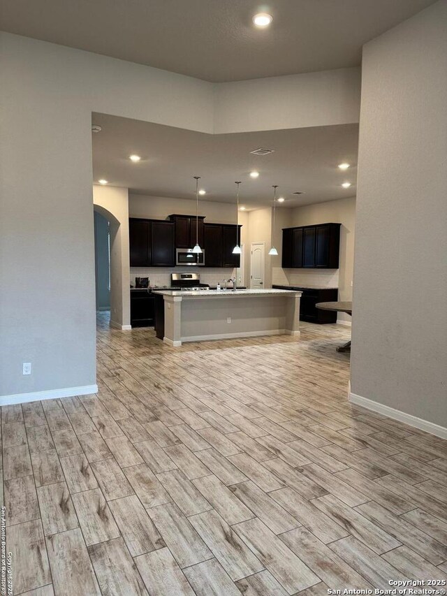 kitchen featuring arched walkways, stainless steel appliances, wood finish floors, open floor plan, and an island with sink