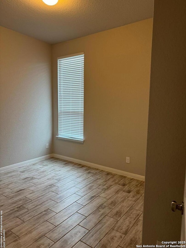 unfurnished room featuring light wood-type flooring, baseboards, and a textured ceiling