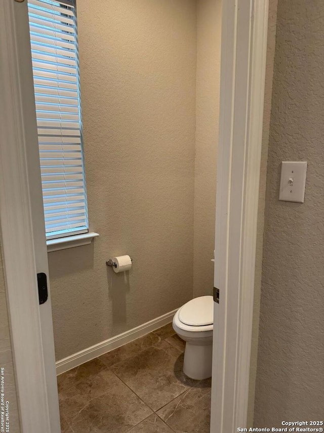 bathroom with baseboards, a textured wall, and toilet