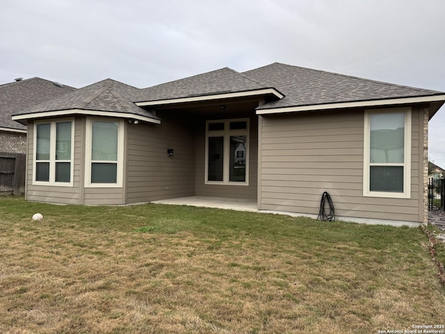 back of property with roof with shingles, fence, a lawn, and a patio