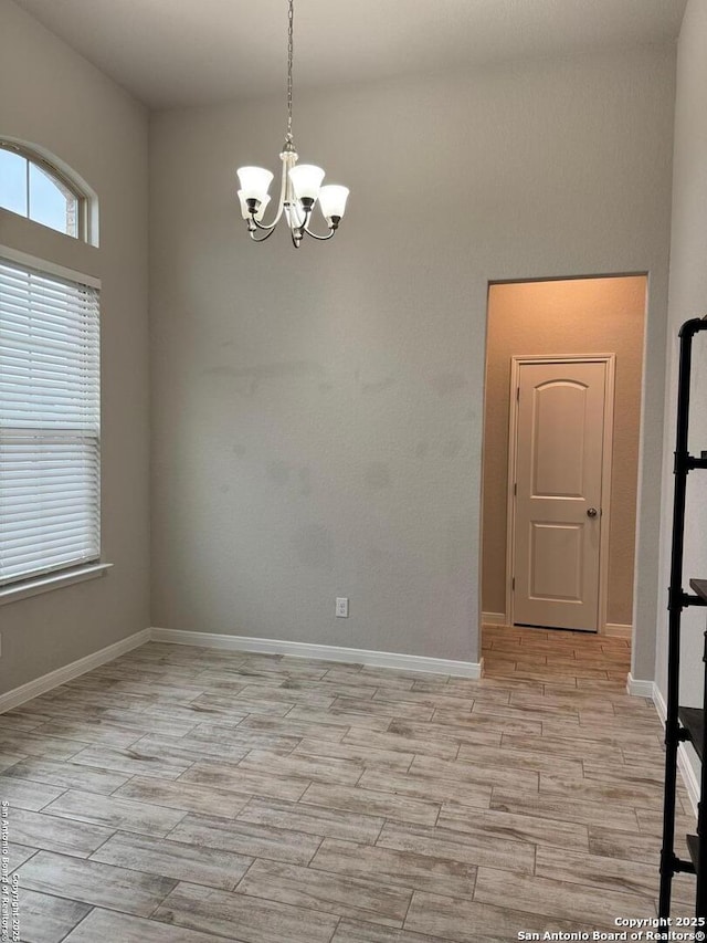 spare room featuring wood finish floors, baseboards, and an inviting chandelier