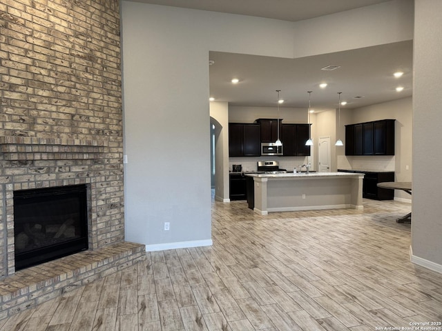 kitchen with a fireplace, stainless steel appliances, light countertops, light wood-style flooring, and open floor plan