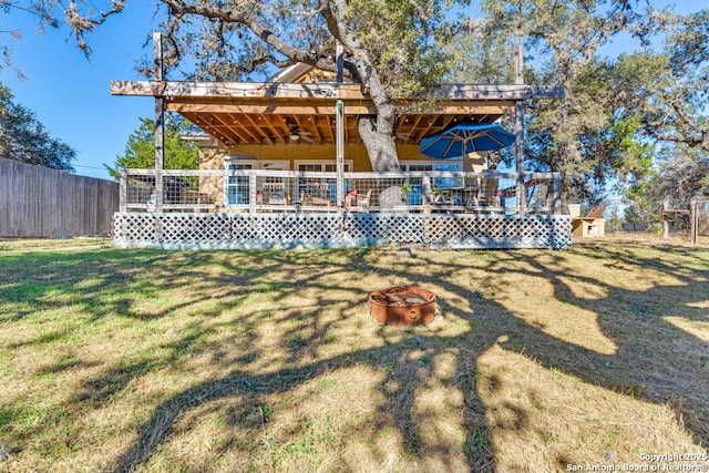 back of house featuring a lawn, a fire pit, and a deck