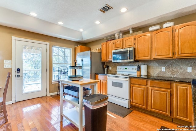 kitchen with decorative backsplash, appliances with stainless steel finishes, light hardwood / wood-style flooring, and dark stone countertops