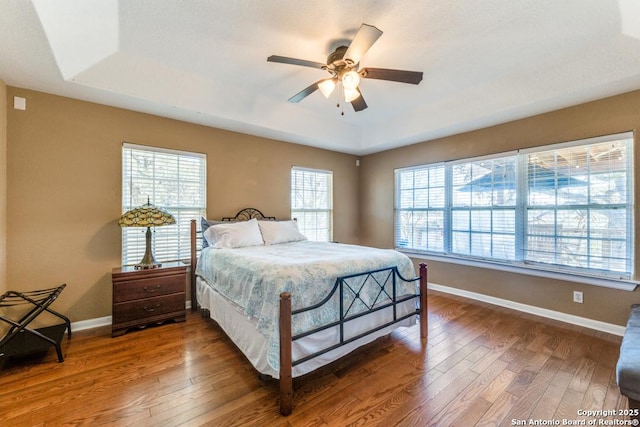 bedroom with multiple windows, wood-type flooring, a raised ceiling, and ceiling fan