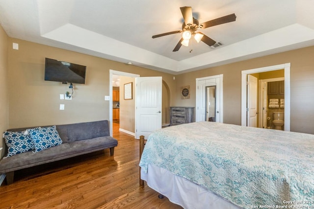 bedroom featuring ensuite bath, a raised ceiling, ceiling fan, and hardwood / wood-style flooring