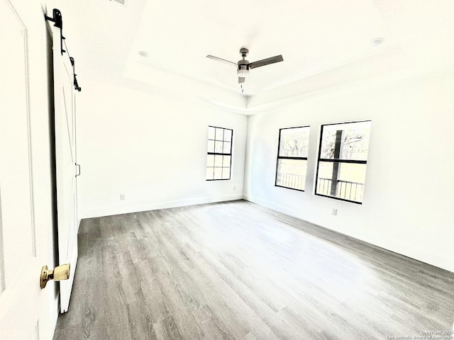 empty room with ceiling fan, a raised ceiling, and light hardwood / wood-style flooring