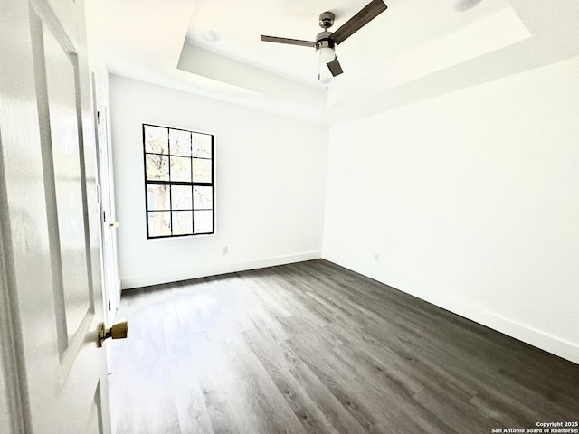 unfurnished room with a tray ceiling, ceiling fan, and dark hardwood / wood-style floors