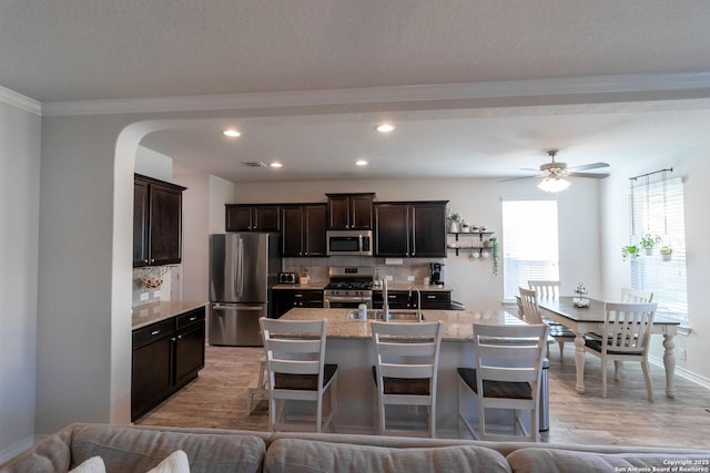 kitchen with tasteful backsplash, appliances with stainless steel finishes, a center island with sink, and light wood-type flooring