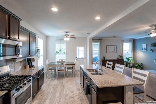 kitchen with sink, a breakfast bar area, stainless steel appliances, light stone countertops, and a kitchen island with sink