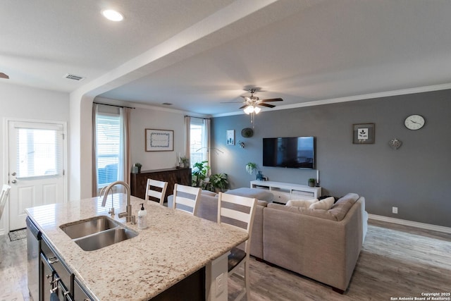 kitchen with sink, light stone counters, light wood-type flooring, dishwasher, and a kitchen island with sink