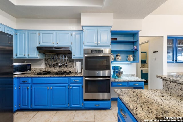 kitchen featuring blue cabinets, decorative backsplash, light tile patterned flooring, light stone counters, and stainless steel appliances