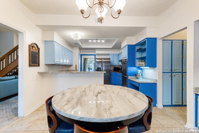 kitchen with black double oven, stainless steel refrigerator with ice dispenser, blue cabinetry, a tray ceiling, and a chandelier