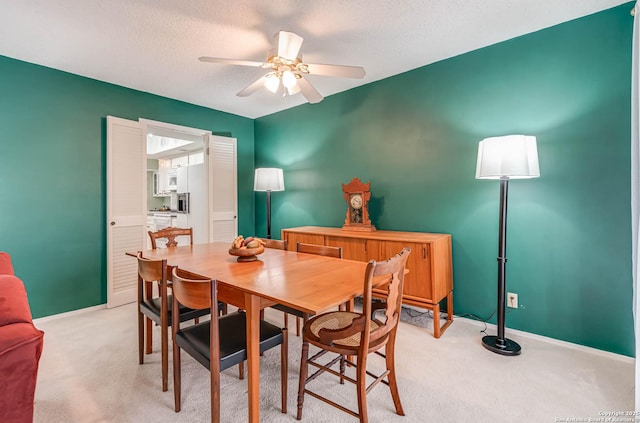 dining space featuring ceiling fan, light colored carpet, and a textured ceiling