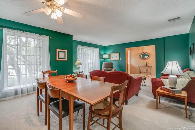 dining area featuring light carpet, ceiling fan, and a textured ceiling