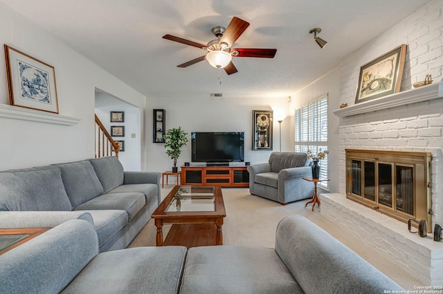 living room with ceiling fan, a brick fireplace, and a textured ceiling