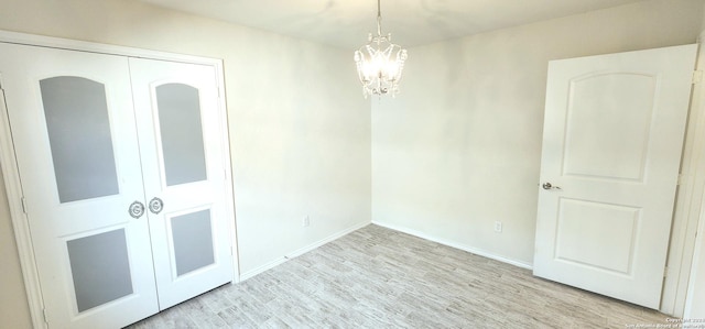 empty room with light hardwood / wood-style flooring and an inviting chandelier