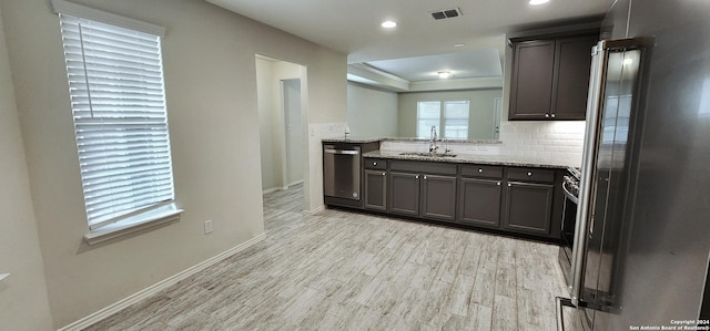 kitchen with sink, light stone countertops, appliances with stainless steel finishes, tasteful backsplash, and light hardwood / wood-style floors